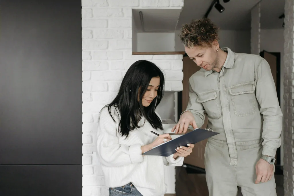 Two colleagues, a man and a woman, standing together in a modern office and reviewing information on a tablet.