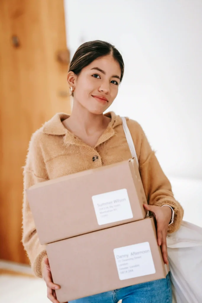 A smiling woman standing and holding two small cardboard shipping boxes ready for delivery.