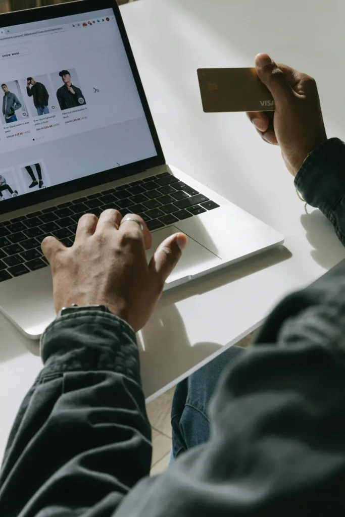 A person making an online purchase by looking at an e-commerce site on a laptop while holding a credit card.